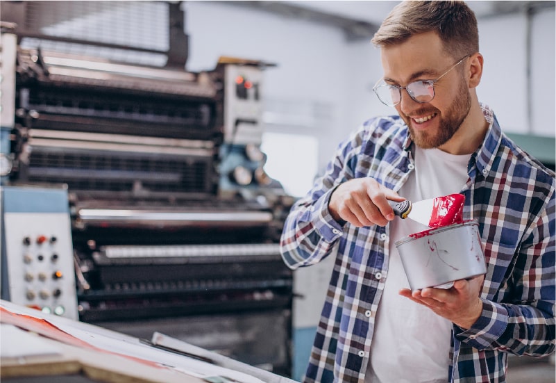A man is smiling and doing screen printing for an apparel company