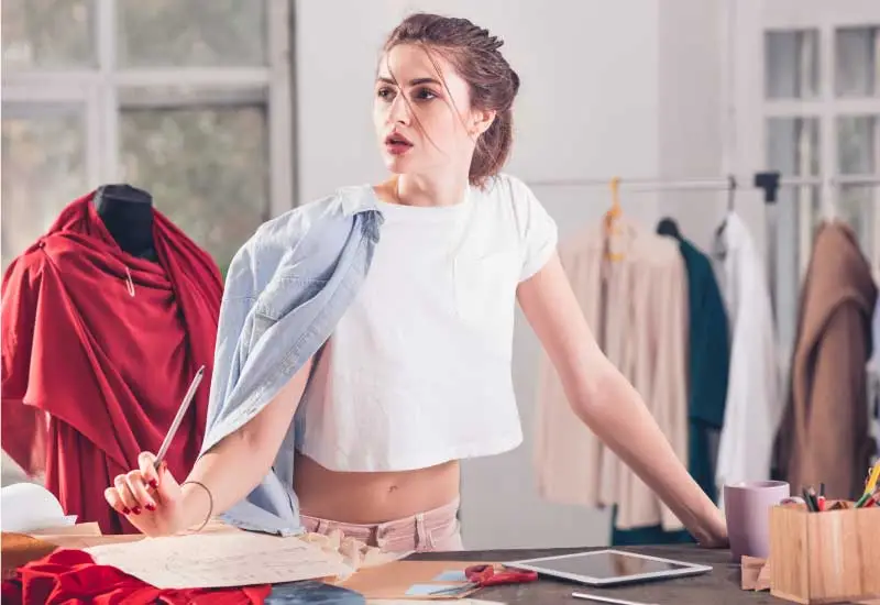 A person working on a fashion design project in a studio with scissors, fabric, and clothing rack 